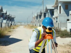 Local surveyor performing land measurements at a residential development site with newly built homes in the background