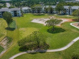 Aerial view of apartment community green space, walking paths, playground, pond, and planned amenity area in Hollywood, Florida.