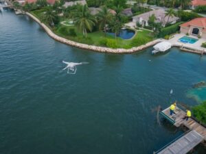Drone conducting an aerial survey over a waterfront property while land surveyors inspect a dock and shoreline conditions for coastal planning in Hollywood, Florida.